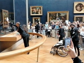 Museum staff clean the protective glass with da Vinci's Mona Lisa behind it, after a visitor smeared it with cream, in Paris, France Sunday, May 29, 2022 in this screen grab obtained from a social media video.