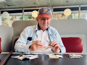 Man sits at table with money and notes, holding note that reads 'love every body'