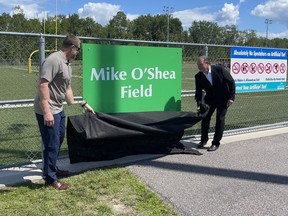 Winnipeg Blue Bombers head coach Mike O'Shea (left) helps North Bay Mayor Al McDonald uncover the sign for Mike O'Shea Field in his hometown of North Bay, Ont., on Saturday, Aug. 13, 2022. The City of North Bay is dedicated the football field in his honour of the CFL Hall of Famer and two-time Grey Cup winning coach.