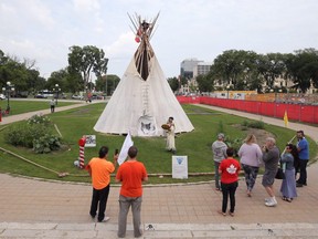 A woman plays a drum song and a man sits in the top of a tipi in an encampment on the Manitoba Legislative Building grounds in Winnipeg on Tues., Aug. 23, 2022.