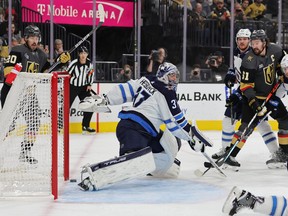 The puck ricochets off of a goal post as Connor Hellebuyck of the Winnipeg Jets defends the net against the Vegas Golden Knights.