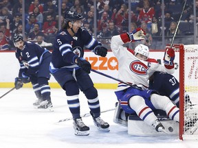 Montreal Canadiens center Nick Suzuki (14) slides into Winnipeg Jets goaltender Connor Hellebuyck (37) after his first-period goal.