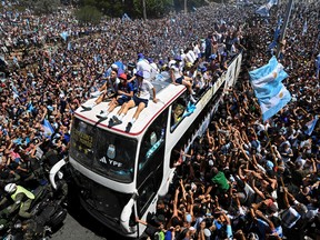 TOPSHOT - Fans of Argentina cheer as the team move aboard a bus after winning the 2022 Qatar World Cup tournament in Buenos Aires, Argentina December 20, 2022. - Millions of adoring fans are expected to cheer for their heroes as Argentina's world champions led by captain Lionel Messi began their open-top bus parade in the capital Buenos Aires on Tuesday after their sensational victory over France. (Photo by Luis ROBAYO/AFP) (Photo by LUIS ROBAYO/AFP via Getty Images)
