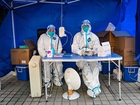 TOPSHOT - Health workers wait for people to scan a health code to test for the Covid-19 coronavirus in the Jing'an district in Shanghai on December 22, 2022.