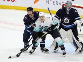 Winnipeg Jets defenceman Neal Pionk (left) ties up Seattle Kraken centre Karson Kuhlman in front of goaltender Eric Comrie in Winnipeg on Sun., May 1, 2022.  KEVIN KING/Winnipeg Sun/Postmedia Network