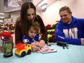 Winnipeg Blue Bombers linebacker Adam Bighill (right) watches as wife Kristina helps their 3-year-old son Beau sign an autograph at Red River Co-op on Vermillion Road in Winnipeg on Sun., Dec. 11, 2022. The Bighills helped sell the Kids Holiday Favourite Cookbook, for a minimum $5 donation, with proceeds going to Child Life Programs through the Children's Hospital Foundation of Manitoba.