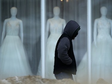 A person wears a mask while walking past a window display of dresses in Winnipeg on Wednesday, Feb. 9. 2022.