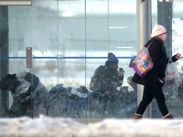 A person wears a mask while walking past a filthy, garbage strewn bus shack where people are eating, resting, and smoking an unknown substance from a glass pipe in Winnipeg on Saturday, Jan. 15, 2022.
