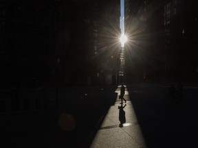 Pedestrians walk through a sliver of sunlight in the financial district in downtown Toronto on Wednesday July 6, 2022.