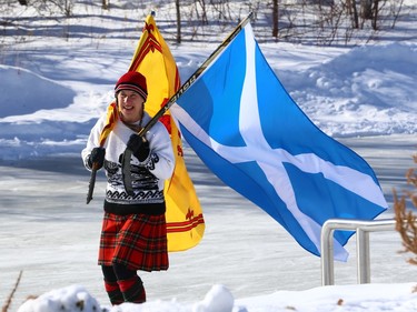 A woman wearing a kilt carries two Scottish flags during the Great Canadian Kilt Skate on the duck pond at Assiniboine Park in Winnipeg on Sunday, Feb. 26, 2023.