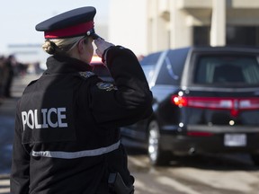 An Edmonton Police Service officer salutes as a procession arrives with the bodies of Const. Travis Jordan and Const. Brett Ryan at the Serenity Funeral Home in Edmonton Tuesday, March 21, 2023.