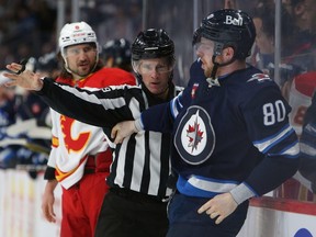 A linesman separates Pierre-Luc Dubois of the Winnipeg Jets and Chris Tanev of the Calgary Flames in the second period during a game on April 5, 2023 at Canada Life Centre in Winnipeg.