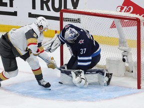 Connor Hellebuyck of the Winnipeg Jets makes a save on Brett Howden of the Vegas Golden Knights.