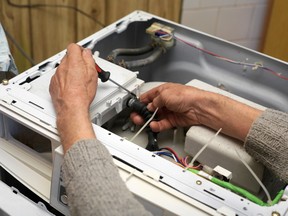 Service man with a screwdriver repairing a washing machine.