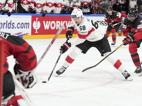 Fabrice Herzog, of Switzerland, centre, fights for a puck with Pierre-Olivier Joseph, of Canada, during the hockey world championship in Riga, Latvia, Saturday, May 20, 2023.
