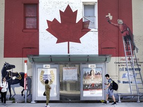 People wait at a bus stop in with a huge mural of a Canadian flag being painted by a Mountie, Thursday June 29, 2023.