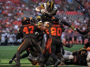 Hamilton Tiger-Cats running back James Butler jumps over BC Lions' defenders Sione Teuhema and Boseko Lokombo to score a touchdown during first half of Saturday's game at B.C. Place.