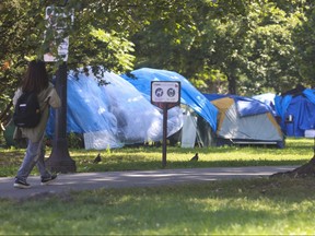 A person walks through the massive homeless encampment at Allan Gardens in Toronto with too many tents and structures to count on Tuesday Aug. 22, 2023.