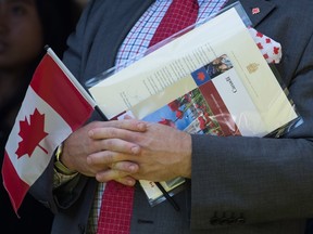 A new Canadian holds a Canadian flag, their citizenship certificate and a letter signed by Prime Minister Justin Trudeau after becoming a Canadian citizen, during a special Canada Day citizenship ceremony in West Vancouver on Monday, July 1, 2019.