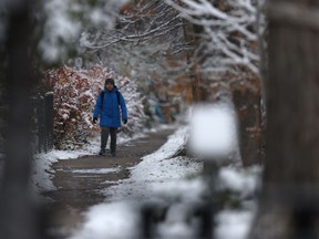 A person walks along a sidewalk surrounded by the first snow of the season
