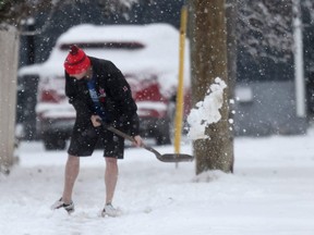 A man wearing shorts shovels snow
