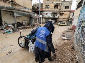 A man collects trash while wearing a jacket bearing the logo of the United Nations Relief and Works Agency for Palestine Refugees in the Near East (UNRWA), along a street in the city of Jenin in the occupied West Bank on Jan. 30, 2024.