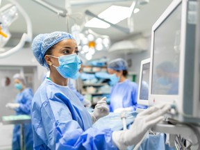 Anesthetist Working In Operating Theatre Wearing Protecive Gear checking monitors while sedating patient before surgical procedure in hospital