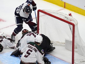 Colorado Avalanche centre Nathan MacKinnon, top, pushes the puck past Arizona Coyotes goaltender Karel Vejmelka for a goal as Coyotes defenceman Michael Kesselring watches in the second period of an NHL hockey game Sunday, Feb. 18, 2024, in Denver. (AP Photo/David Zalubowski)