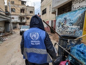 A man collects trash while wearing a jacket bearing the logo of the United Nations Relief and Works Agency for Palestine Refugees in the Near East (UNRWA), along a street in the city of Jenin in the occupied West Bank, Tuesday, Jan. 30, 2024.