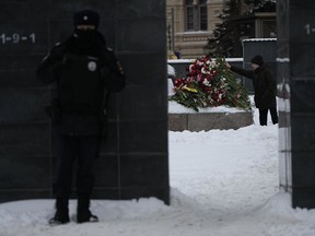 A policeman guards as a young man lay flowers paying the last respect to Alexei Navalny at the monument, a large boulder from the Solovetsky islands, where the first camp of the Gulag political prison system was established, near the historical the Federal Security Service (FSB, Soviet KGB successor) building, in Moscow, Russia, on Saturday morning, Feb. 17, 2024.
