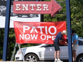 Two people work to install a "Patio Open" sign