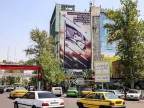 Vehicles move past a building showing a banner depicting missiles and drones flying past a torn Israeli flag, with text in Persian reading "the next slap will be harder" and in Hebrew "your next mistake will be the end of your fake state," in Palestine Square in Tehran on April 14, 2024.