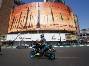 A man rides a motorbike past a billboard depicting Iranian ballistic missiles in service in Tehran on April 19, 2024.