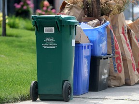 A green bin lined up with garbage and recycling bins