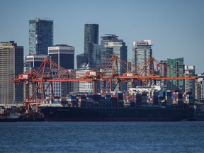 A container ship docked under gantry cranes at port and the downtown skyline are seen in Vancouver